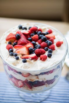 a dessert with strawberries, blueberries and cream in a glass dish on a table