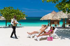 a man standing next to a woman laying on top of a white lawn chair in front of the ocean