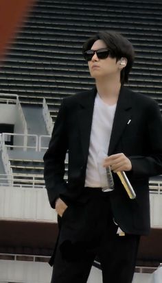 a man wearing sunglasses and a black suit stands in front of an empty bleachers