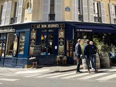 two men are walking down the street in front of a building with shops on it