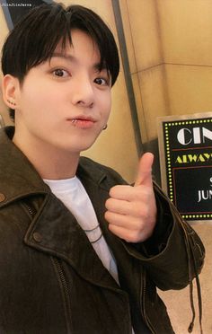 a young man giving the thumbs up sign in front of a movie theater entrance with a chalk board behind him