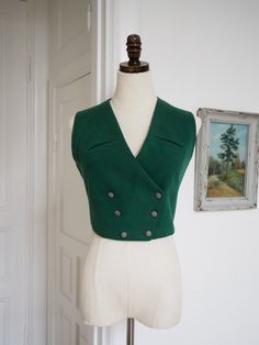 Dark green wool 1940s waistcoat with breast pockets. Double breasted and closes with dressed buttons. Such a stunner that will take any outfit to the next (very dapper!) level. Measurements: Bust 86 cm/ 33.8" Waist 70 cm/ 27.5" Length (at middle back) 40 cm/ 15.7" Excellent condition. Shows some wear to the neck of lining. Fitted Green Vest With Button Closure, Green Buttoned Vest For Workwear, Green Fitted Classic Vest, Vintage Buttoned Vest For Workwear, Vintage Vest With Buttons For Workwear, Vintage Workwear Vest With Buttons, Vintage Formal Winter Vest, Retro Fitted Sleeveless Outerwear, Elegant Green Workwear Vest