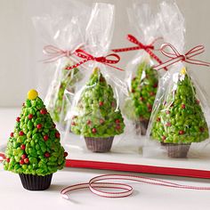 three small christmas trees in plastic bags on a white table with red and green ribbon