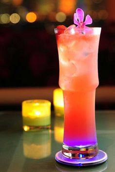 a tall glass filled with ice and topped with a pink flower sitting on top of a table