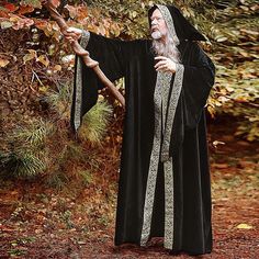 an old man dressed in black and holding a stick with his right hand while standing next to a tree