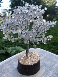 a small silver tree sitting on top of a wooden table next to a green bush