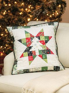 a christmas pillow sitting on top of a white chair next to a tree with lights