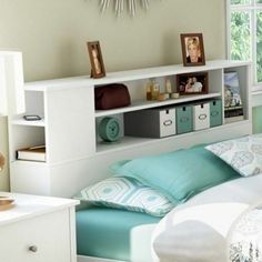 a white bed sitting under a window next to a shelf filled with pictures and other items