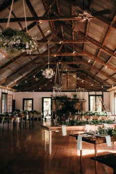 an indoor wedding venue with wooden tables and chandeliers hanging from the ceiling, surrounded by greenery