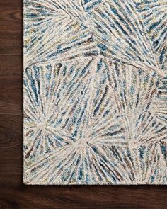 a white rug with blue and green designs on top of a wooden floor next to a wall