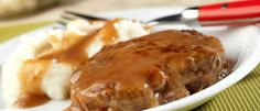 a white plate topped with meat and gravy covered in gravy next to mashed potatoes