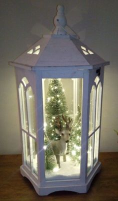 a small white lantern with a deer in it and christmas trees inside the lantern holder