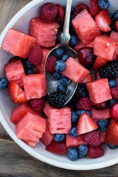 a bowl filled with watermelon, raspberries and blueberries next to a spoon