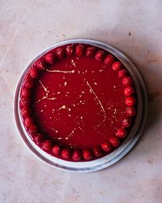 a cake with red icing and raspberries on it sitting in a metal pan