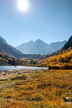 the sun shines brightly in the mountains above a river surrounded by grass and trees