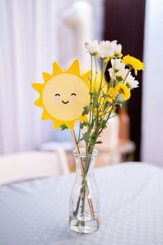 a vase filled with yellow and white flowers on top of a blue table cloth covered table