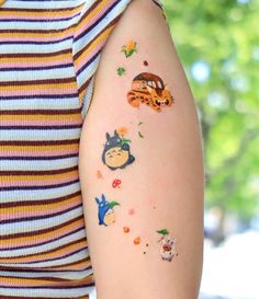 a woman's arm with tattoos on it, including an image of the characters from totoro