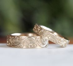 two wedding rings sitting on top of a white table next to each other with green plants in the background