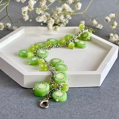 a bracelet with green beads and kiwis is sitting on a tray next to flowers