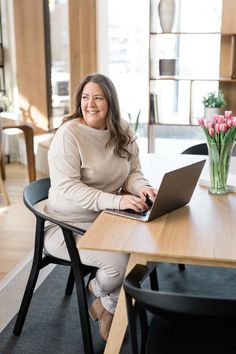 a woman sitting at a table with a laptop in front of her, smiling for the camera