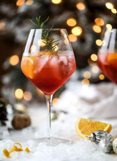 two wine glasses filled with red liquid and garnished with rosemary, sitting on snow