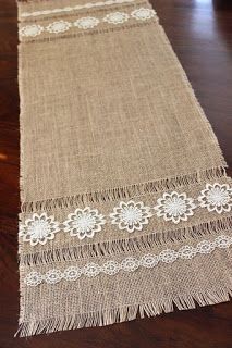 a table runner with white lace and flowers on it, sitting on a wooden floor