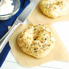 two bagels sitting on top of parchment paper next to a bowl of whipped cream