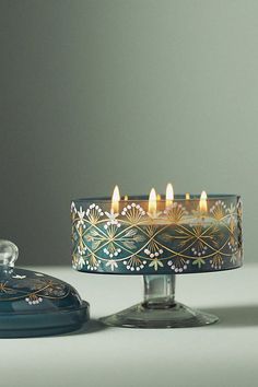 a lit candle sitting on top of a table next to a glass container filled with candles