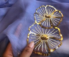 a hand holding two pieces of gold and white beaded broochies on top of a blue cloth