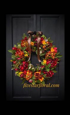 a wreath is hanging on the front door with flowers and leaves around it in red, orange, yellow and green colors