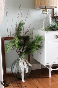 a vase with pine branches in it sitting on a table next to a white dresser