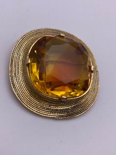 "Vintage Accessocraft NYC pin brooch. Gold tone with a large, yellow topaz colored faceted glass stone. Setting features a delicate rope texture. The glass gem is topaz yellow color with a wide streak of darker  amber orange color in center. Surface of glass gem is free of scratches. Brooch is marked \"ACCESSOCRAFT N.Y.C.\" A unique, show stopping statement piece!" Antique Gold Brooch With Gemstone, Antique Gold Gemstone Brooch, Yellow Brooch For Formal Occasions, Formal Gold Gemstone Brooches, Gold Gemstone Round Brooch, Gold Gemstone Round Brooches, Round Gold Brooch With Gemstone, Round Gold Brooches With Gemstone, Gold Jeweled Costume Jewelry Brooches