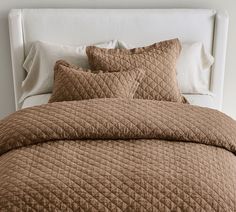 a bed with brown quilted bedspread and pillows on it's headboard