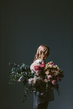 a woman holding a bunch of flowers in her hands and looking down at the ground