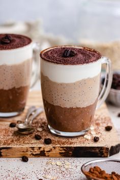 two mugs filled with chocolate and coffee on top of a cutting board next to nuts