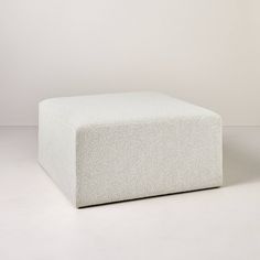 a white square ottoman sitting on top of a white floor next to a gray wall