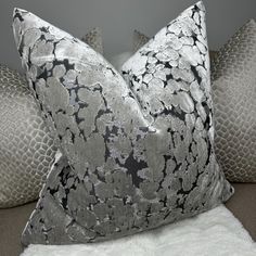 a silver and black pillow sitting on top of a white couch next to two pillows