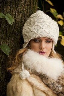 a woman wearing a white hat and fur coat next to a tree with leaves on it