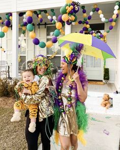 two women and a baby are dressed up for mardi gras in front of a house