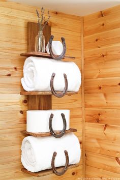 two towel racks with horseshoes on them in a wooden cabin bathroom, one is made out of wood and the other has three white towels