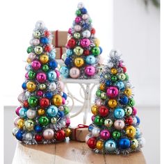 two small christmas trees made out of ornaments on top of a wooden table next to a chair