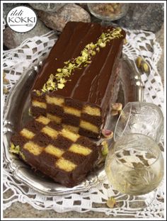 a chocolate cake on a glass plate next to a wine glass and some nuts in the background