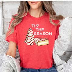 a woman wearing a red tis the season t - shirt with a cake on it