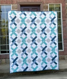 a blue and gray quilt hanging from the side of a brick building in front of a door