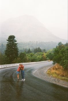 two people hugging each other on the side of a road with mountains in the background