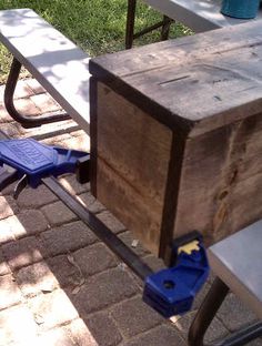 a wooden box sitting on top of a sidewalk next to a blue toolbox and some chairs