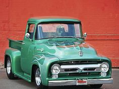 an old green truck parked in front of a red wall