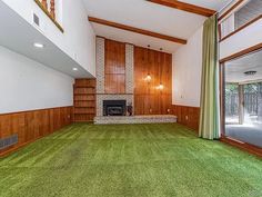 an empty living room with wood paneling and green carpet