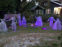 some purple plastic figures in the grass near a fence and house with lights on it