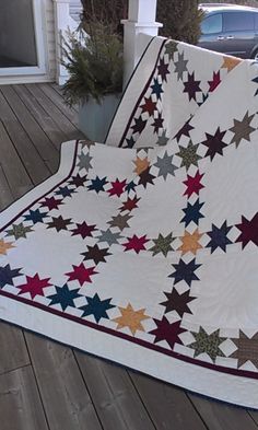 a large white quilt with stars on it sitting on a porch next to a car